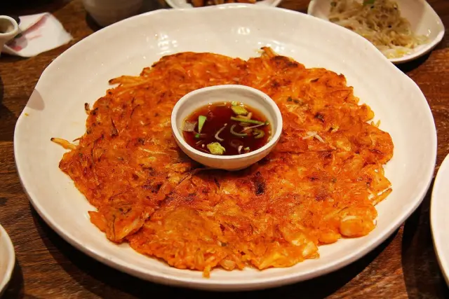 A crisp kimchi pancake on a white plate with dipping sauce