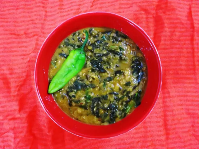 Red lentil dal with spinach in a red bowl, topped with a green chilli